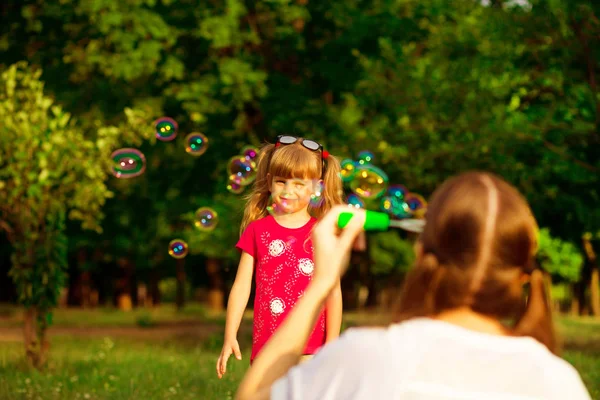 Junge Mutter und kleine Tochter spielen im Park mit Seifenblasen. Liebe Familie, Elternschaft, Kindheit — Stockfoto
