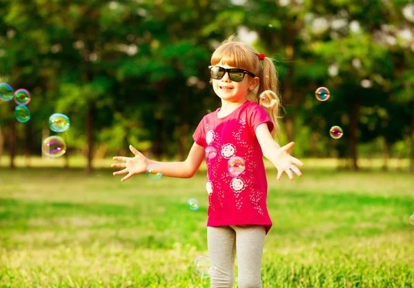 Feliz niña rubia sopla burbujas de jabón en el parque de verano —  Fotos de Stock