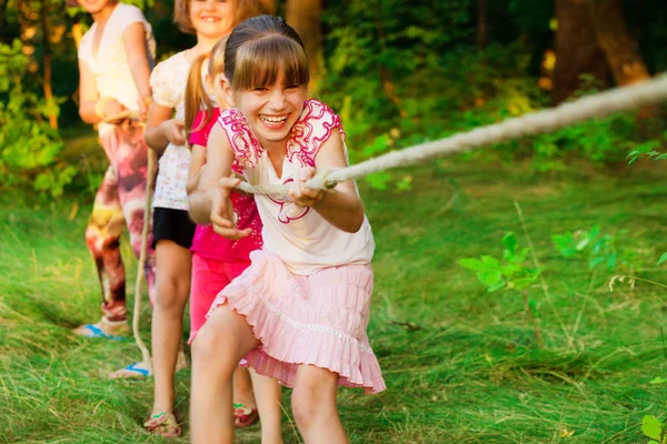 Grupp med glada barn som leker dragkamp utanför på gräs. Barnen dra rep på park. — Stockfoto