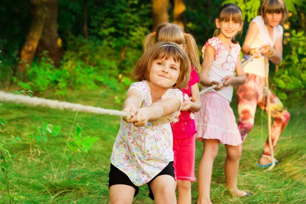 Gruppe fröhlicher Kinder, die draußen im Gras Tauziehen spielen. Kinder ziehen Seil im Park. — Stockfoto