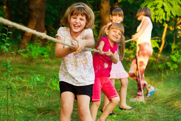 Grupp med glada barn som leker dragkamp utanför på gräs. Barnen dra rep på park. — Stockfoto