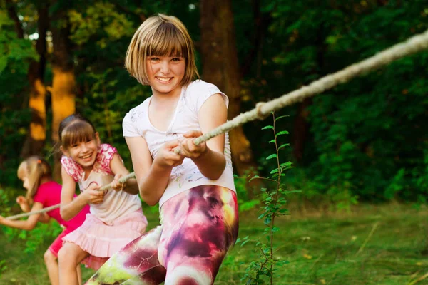 Group of happy children playing tug of war outside on grass. Kids pulling rope at park. — Stock Photo, Image