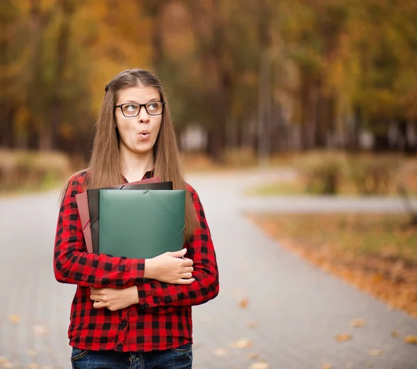 Joven estudiante con la cara sorprendida se ve fuera de la carpeta en camisa a cuadros rojo. Retrato de una joven inteligente sosteniendo carpetas —  Fotos de Stock