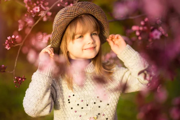 Retrato da mola, menina adorável no passeio do chapéu no jardim da árvore da flor no por do sol — Fotografia de Stock