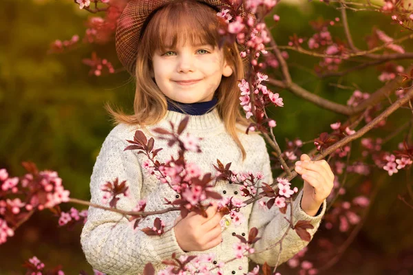 Весняний портрет, чарівна маленька дівчинка в капелюсі гуляє в квітучому саду на заході сонця — стокове фото