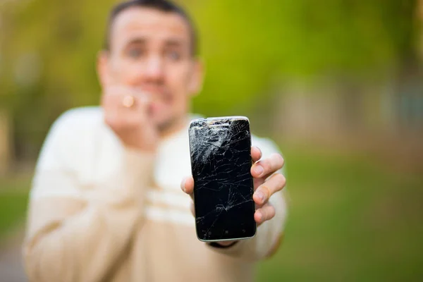 Joven guapo sostiene la pantalla rota del teléfono inteligente estresado con la mano en la cabeza, sorprendido con la vergüenza y la cara sorpresa, enojado y frustrado . — Foto de Stock