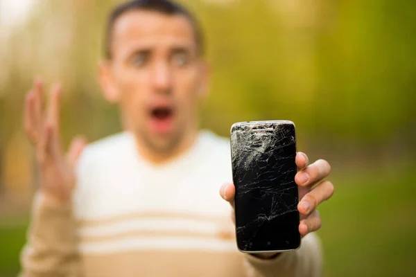 Handsome young man hold broken smartphone screen stressed with hand on head, shocked with shame and surprise face, angry and frustrated. — Stock Photo, Image
