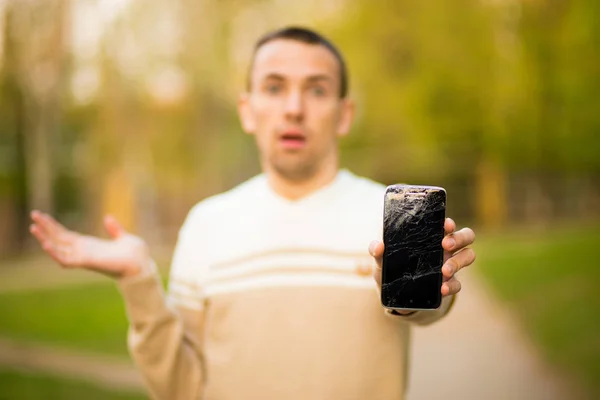 Joven guapo sostiene la pantalla rota del teléfono inteligente estresado con la mano en la cabeza, sorprendido con la vergüenza y la cara sorpresa, enojado y frustrado . — Foto de Stock