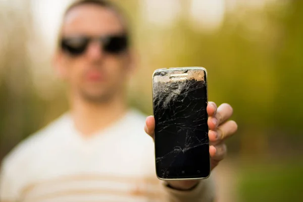 Tipo sosteniendo teléfono inteligente negro con pantalla rota. Pantalla rota del teléfono moderno sin marco . — Foto de Stock