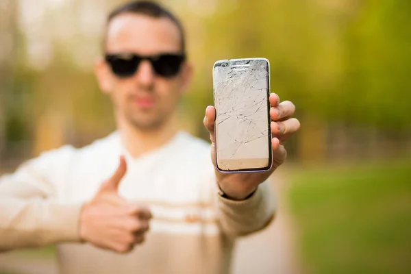 Handsome young man showing broken smartphone screen doing ok sign, thumb up with fingers — Stock Photo, Image