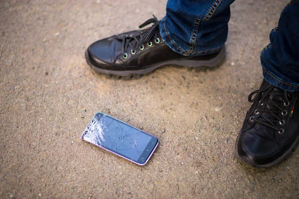 Persona que recoge el teléfono inteligente roto con la pantalla agrietada en tierra — Foto de Stock