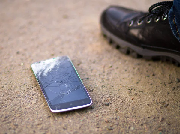 Persona que recoge el teléfono inteligente roto con la pantalla agrietada en tierra — Foto de Stock