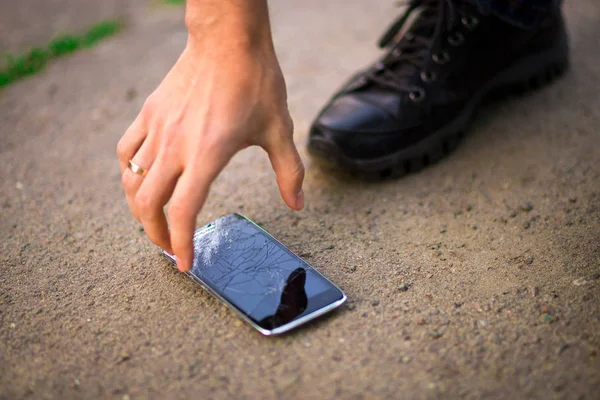 Persona que recoge el teléfono inteligente roto con la pantalla agrietada en tierra — Foto de Stock