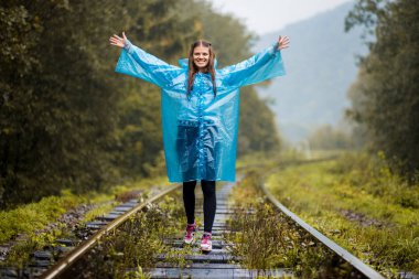 Kız Gezgin giyiyor mavi ceket ve go orman tren tarafından. Mavi yağmur ceket kız ormanda, sis yürür iken koyu yeşil tonları ile sonbahar, yağmur sezonu