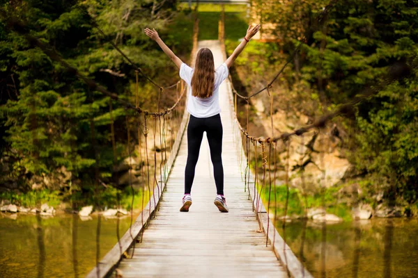 Turista mujer caminar por largo puente colgante de madera sobre el río . —  Fotos de Stock