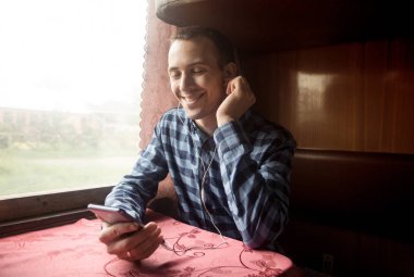 Genç adam trenle seyahat eder ve müzik dinler.