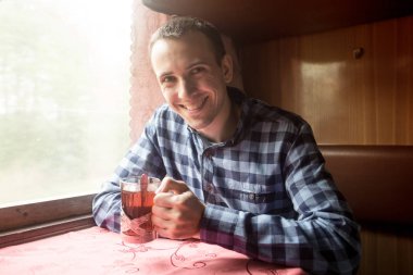 Genç adam sıcak çay içerek trenle seyahat ediyor.