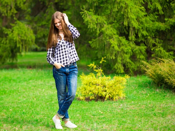 Mladá dívka kráčí podél v bílé bundě a džíny v parku — Stock fotografie