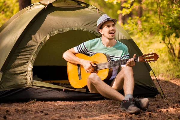 Joven guapo atractivo barbudo modelo hombre en sombrero tocando la guitarra en el bosque . — Foto de Stock