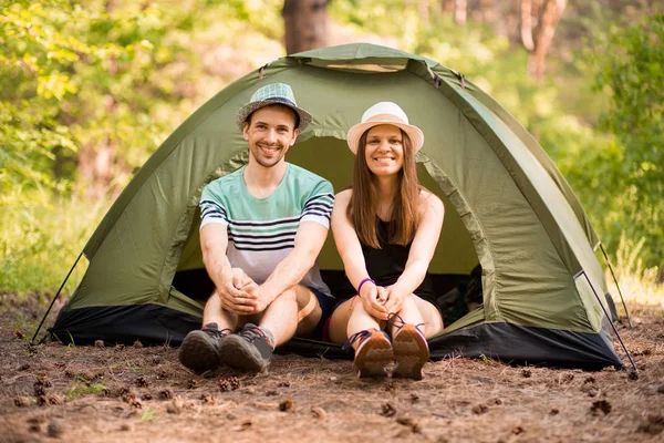 Romantic couple camping outdoors and sitting in tent. Happy Man and woman on romantic camping vacation.
