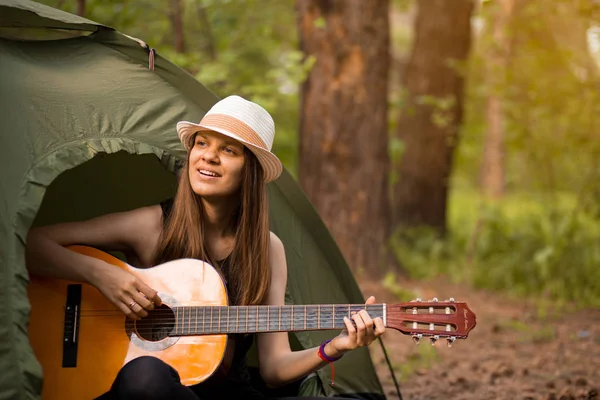 Happy traveler lifestyle woman on vacation camping with tent playing guitar in forest. Travel holiday Concept
