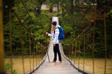 menteşeli köprü ile orman Crossing Nehri'nde yürüyen sırt çantası ile gezgin kadın