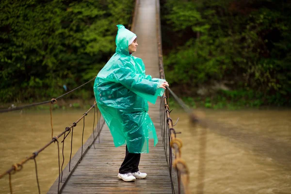 Starszy kobieta 60 lat stary Crossing River przez zawias most w lesie turystyka — Zdjęcie stockowe