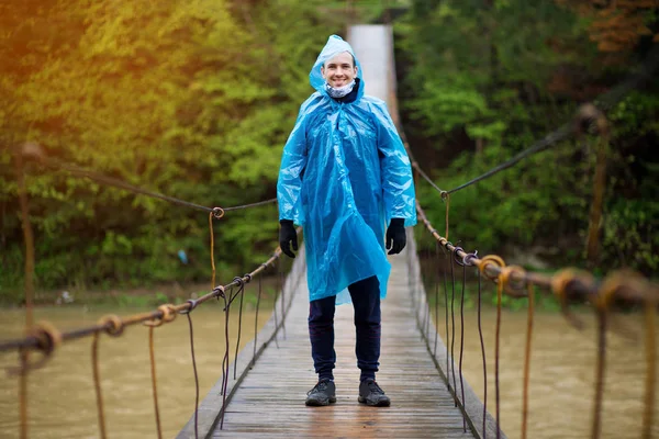 Man in blue raincoat walking in coniferous forest during rainy and foggy day.