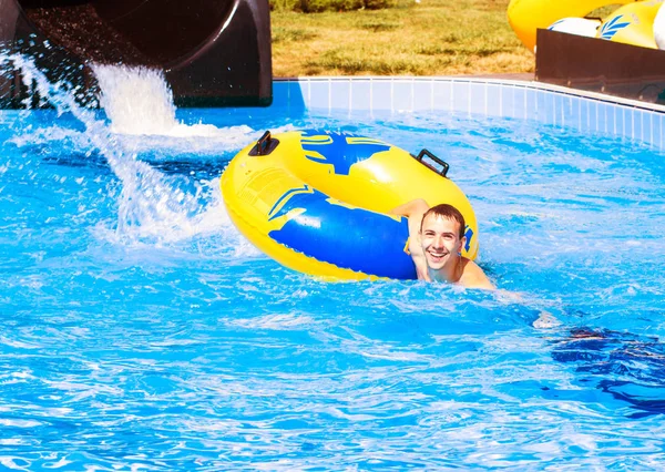 Grappig opgewonden man genieten van zomer vakantie in waterpark paardrijden gele float lachen. — Stockfoto