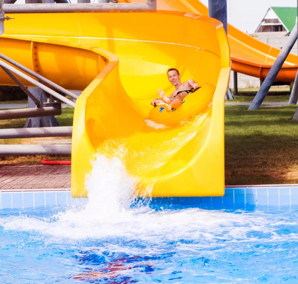 Смішний збуджений чоловік насолоджується літнім відпочинком у аквапарку, катаючись на жовтому плаву сміється . — стокове фото