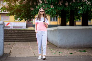 Güneş gözlüğü güzel kız kahve ile yaz sokak tarafından yürümek. Yaşam tarzı kavramı