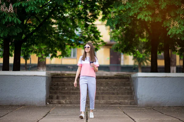 Belle fille en lunettes de soleil marcher dans la rue d'été avec du café. Concept de style de vie — Photo