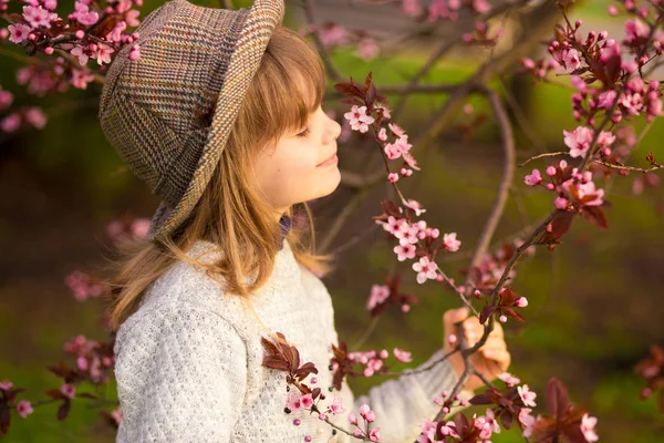 Frühling Porträt, entzückendes kleines Mädchen mit Hut Spaziergang in Blütenbaumgarten bei Sonnenuntergang — Stockfoto