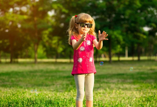 Lindo niño femenino atrapa burbujas de jabón en la naturaleza de verano —  Fotos de Stock