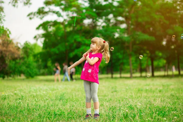 Kleines Mädchen, das auf der Wiese in der Sonne spielt und eine Windmühle in der Hand hält. Kind hält Windspielzeug auf Weizenfeld. — Stockfoto