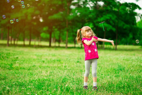 Niña jugando en el prado en el sol con molino de viento en sus manos. Niño sosteniendo juguete de viento en campo de trigo. —  Fotos de Stock