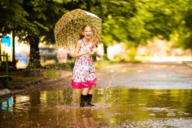 Şemsiye kauçuk çizmeler ve polka nokta elbise ve gülerek su birikintileri üzerinde atlama ile Mutlu komik çocuk kız