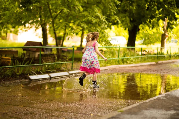 어린 아이 소녀는 웅덩이를 통해 실행됩니다. 여름 야외 — 스톡 사진