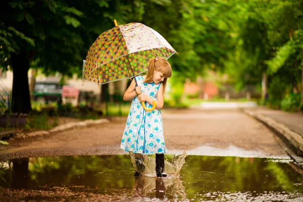 Boldog vicces gyerek lány esernyő jumping a pocsolyákban gumicsizmát és a pöttyös ruha és nevetve — Stock Fotó