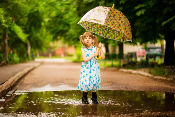 Menina feliz no vestido com um guarda-chuva e botas de borracha na poça no passeio de verão — Fotografia de Stock