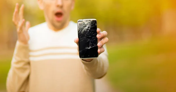 Joven guapo sostiene la pantalla rota del teléfono inteligente estresado con la mano en la cabeza, sorprendido con la vergüenza y la cara sorpresa, enojado y frustrado . — Foto de Stock