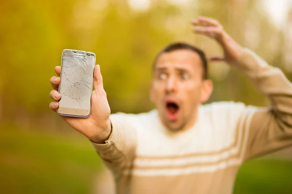 Handsome young man hold broken smartphone screen stressed with hand on head, shocked with shame and surprise face, angry and frustrated. — Stock Photo, Image
