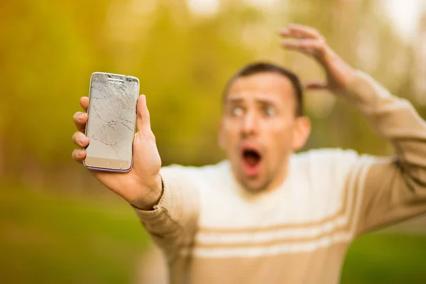 Joven guapo sostiene la pantalla rota del teléfono inteligente estresado con la mano en la cabeza, sorprendido con la vergüenza y la cara sorpresa, enojado y frustrado . — Foto de Stock