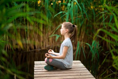 Küçük Kız nehir yakınındaki sahilde gün doğumunda meditasyon
