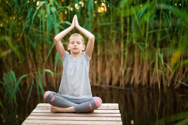 Küçük Kız nehir yakınındaki sahilde gün doğumunda meditasyon