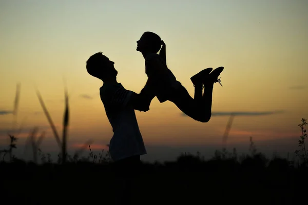 Silhouette of father throwing up his happy daughter in the air at sunset. family time togehter — Stock Photo, Image