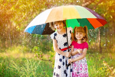Renkli şemsiye sonbahar duş yağmur altında oynayan çocuklarla. Küçük kızlar Yağmurlu hava ile parkta oynamak. Sonbahar açık eğlenceli çocuklar için. Yağmur damlaları yakalamak çocuk.