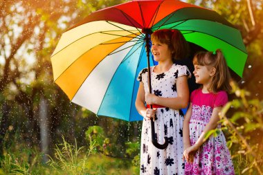 Renkli şemsiye sonbahar duş yağmur altında oynayan çocuklarla. Küçük kızlar Yağmurlu hava ile parkta oynamak. Sonbahar açık eğlenceli çocuklar için. Yağmur damlaları yakalamak çocuk.