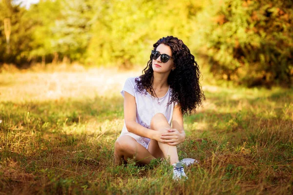 Mooie gekrulde vrouw poseren op gras in zonnige dag — Stockfoto