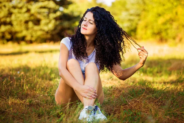 Mooie gekrulde vrouw poseren op gras in zonnige dag — Stockfoto